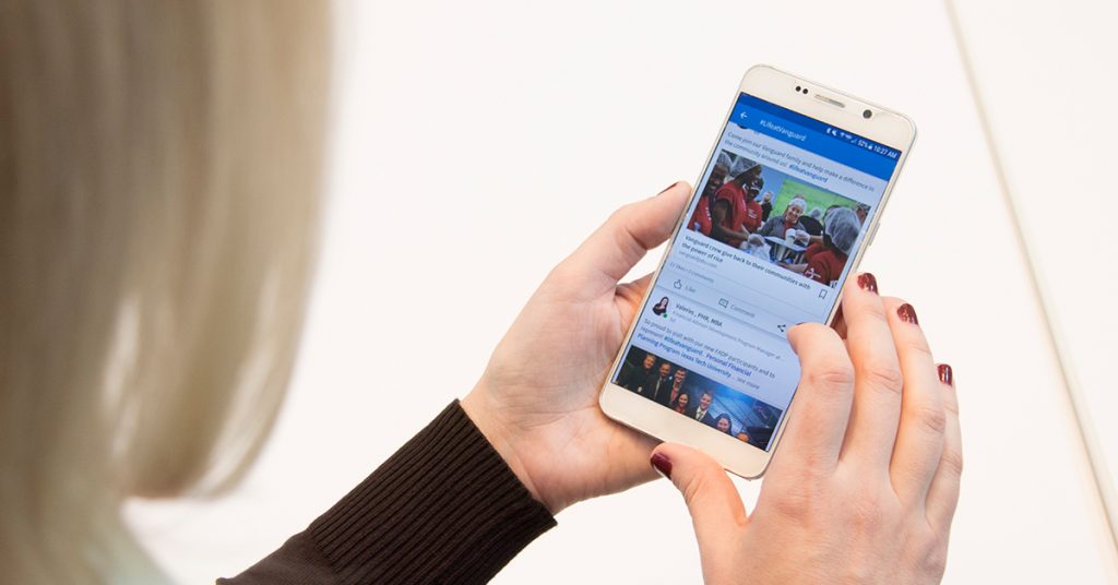 closeup on phone in hands of employee. The phone screen shows the employee's social media feed.