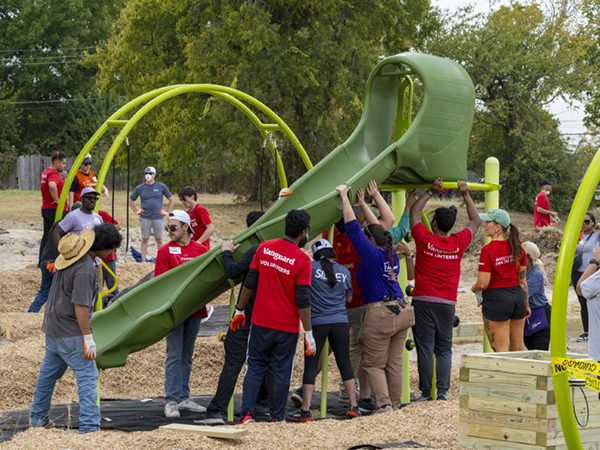 Vanguard Dallas crew volunteers lifting and installing playground equipment during a Kaboom playground build at a local Montessori school.