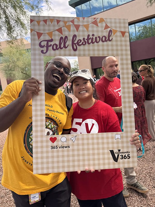 Two people posing together while holding a Fall Festival photo frame at an outdoor Community 365 event.