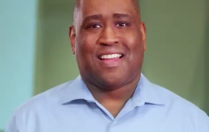 Eric, a recruiter, smiles at the camera in a still from a recruiting video, wearing a light blue button‑down shirt.