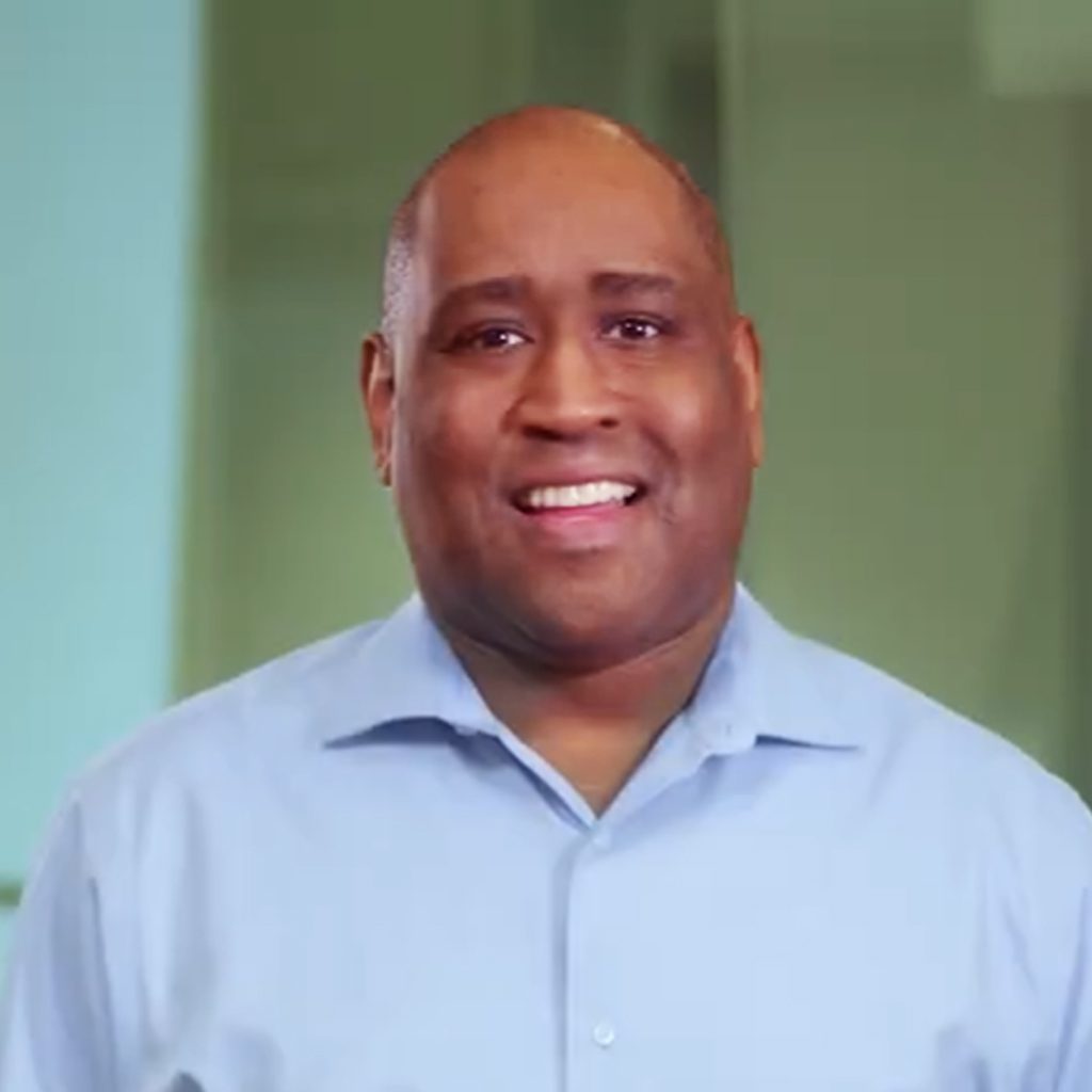 Eric, a recruiter, smiles at the camera in a still from a recruiting video, wearing a light blue button‑down shirt.