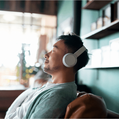 Man seated on a couch with headphones on and eyes closed, looking content.