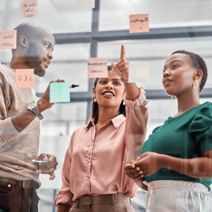 Three coworkers collaborating with sticky notes on a board.