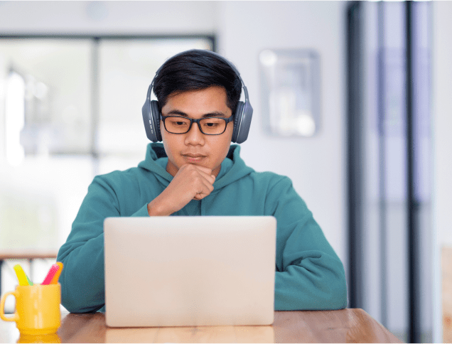 A male student wearing headphones and looking intently at a laptop.
