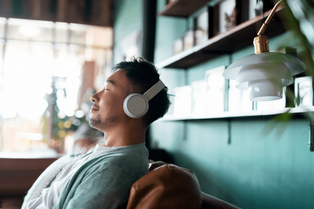 Man seated on a couch with headphones on and eyes closed, looking content.