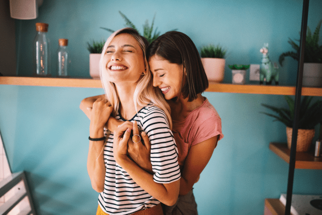 Two young women embracing, looking content in their living room.