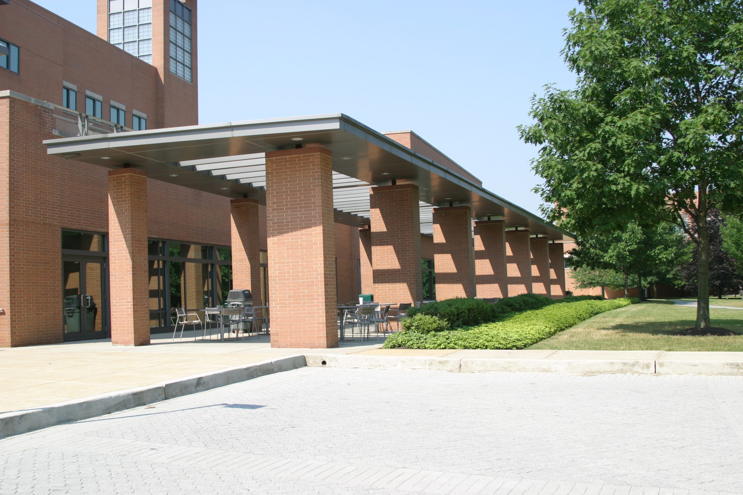 A campus building’s courtyard with outdoor seating and trees on a sunny day.