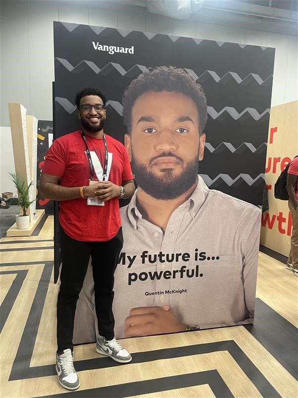 Quentin standing in front of AfroTech booth that features a photo of himself