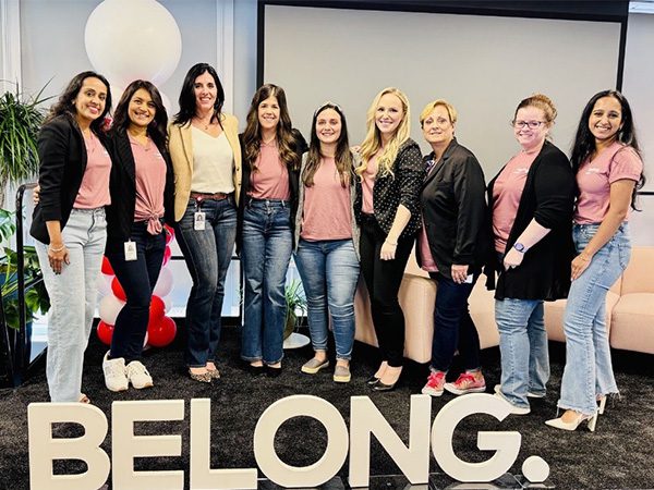 Group photo of Anne and other crew smiling behind an “I Belong” sign at the annual IT WILS Summit.