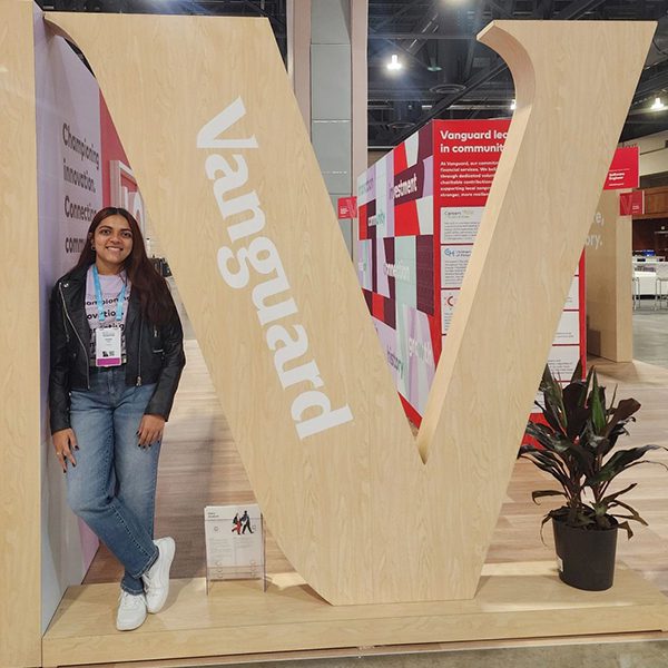 Aashka P. standing next to “V” sign in Vanguard booth at Grace Hopper Conference