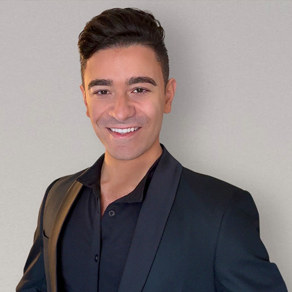 John D. smiling confidently, wearing professional attire against a grey background. 
