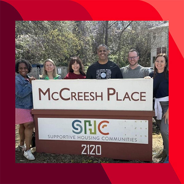 Vanguard_Social_WebContent_Hayley_L_600x600 Haley and five other people stand behind a sign that reads "McCreesh Place" and "Supportive Housing Communities," with the address "2120" at the bottom. Trees and buildings are visible in the background