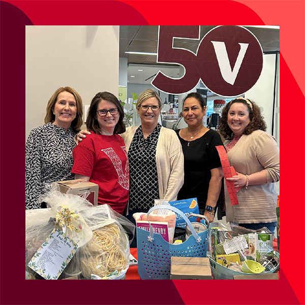 Vanguard_Social_WebContent_Jill_M_600x600 Jill and four other people stand behind a table with various gift baskets, with a large "50V" sign in the background.