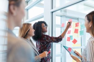 Four teammates participating in a brainstorming activity and ideating with a wall of sticky notes.