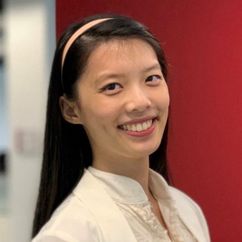 Vanguard recruiter standing indoors in a modern office setting, wearing a black T-shirt with the white text “#LifeatVanguard.” The background shows softly focused office furniture and glass walls, with neutral lighting and a professional workplace environment.