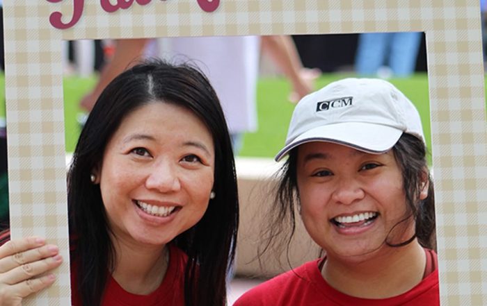 Two people smiling while holding a Fall Festival photo frame during a Community 365 event on a grassy campus area in Arizona