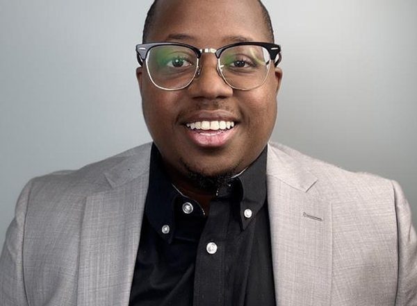 Kenneth in a light gray blazer and black shirt wearing eyeglasses against a neutral background