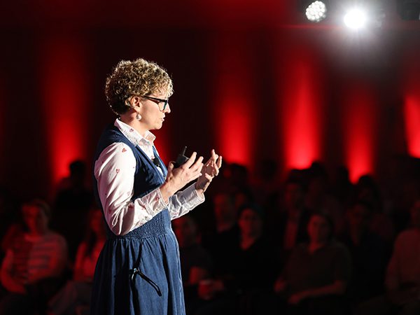 Crew presenter on stage at the unlimITed conference, with dramatic lighting featuring spotlights and red perimeter lighting.